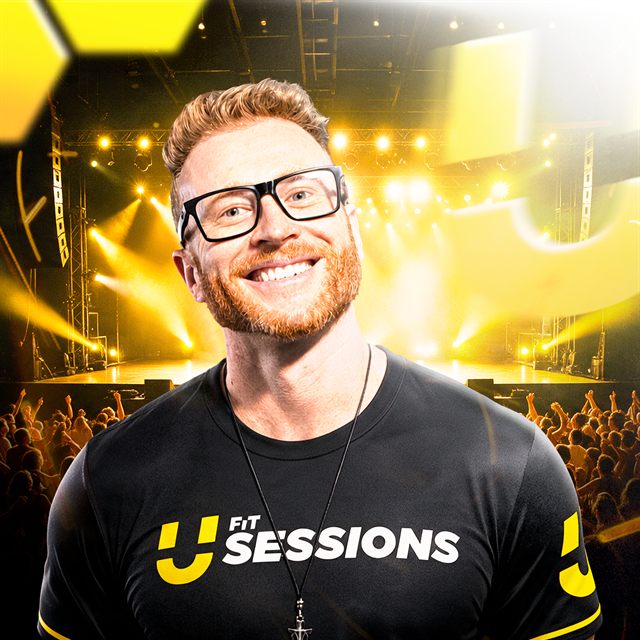 Magno Dutra sorrindo, de óculos e camiseta preta do UFit Sessions, com o palco iluminado ao fundo